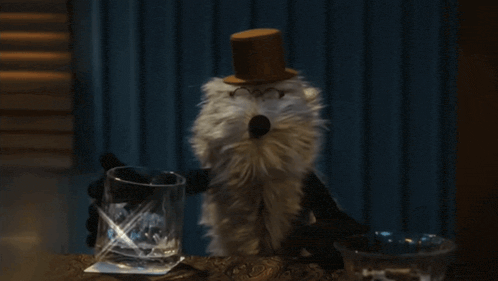 a stuffed animal wearing a top hat and glasses is holding a glass of whiskey