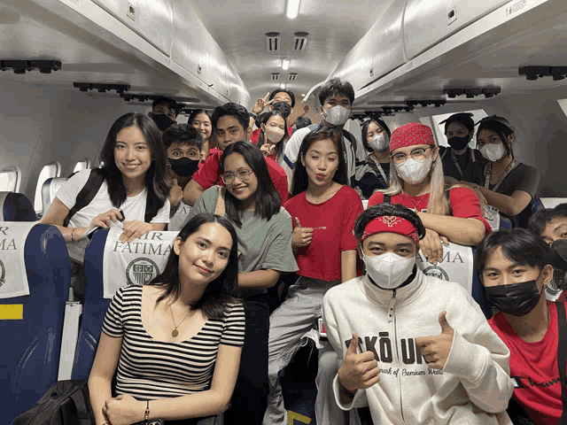 a group of people sitting on a plane wearing masks and a shirt that says kour