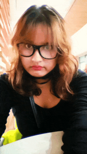 a woman wearing glasses and a choker is sitting at a table