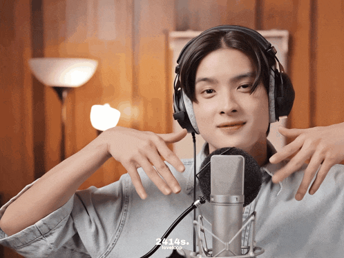 a young man wearing headphones stands in front of a microphone with the number 24146 on the bottom right