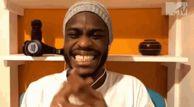 a man wearing headphones and a beanie is smiling in front of a shelf with a mtv logo on it