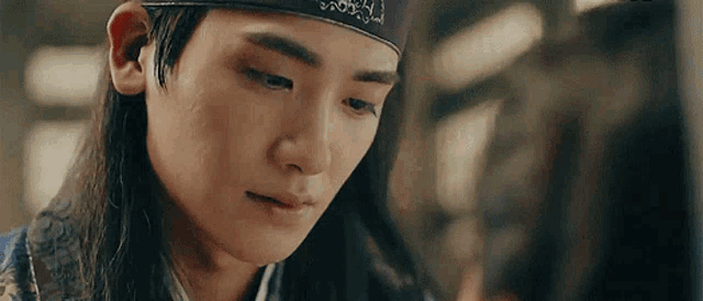a close up of a man with long hair wearing a headband and looking at a woman .