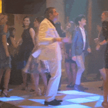 a man in a white suit is dancing on a dance floor with other people