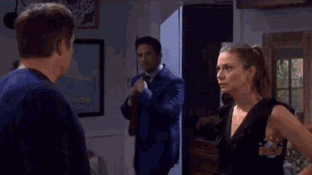 a man in a suit and tie stands next to a woman in a black dress and a man in a blue suit