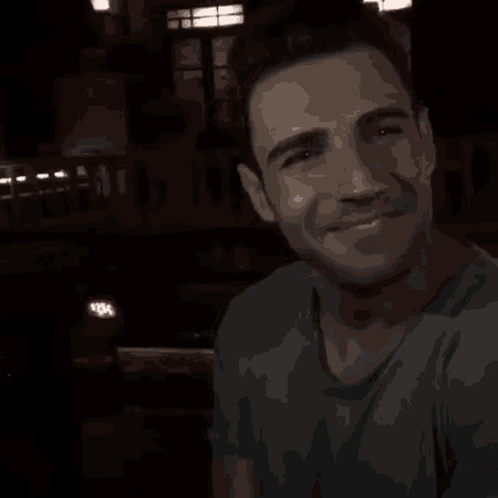 a man is smiling in a dark room while wearing a blue shirt .