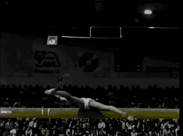 a gymnast performs a trick on a balance beam in front of a crowd of people