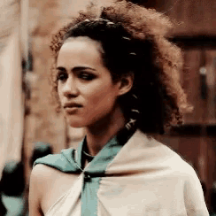 a woman with curly hair and a scarf around her neck is standing in front of a building .