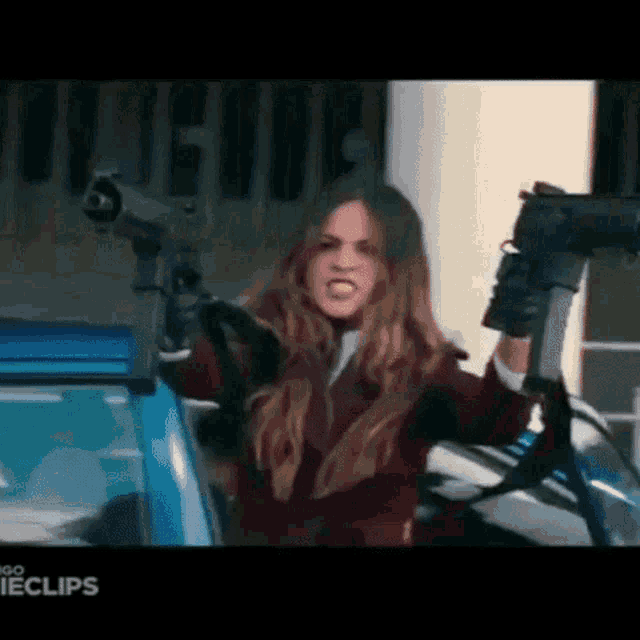 a woman is holding two guns in her hands in front of a car .