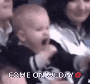 a baby is crying in a crowd of people and a woman is kissing it .