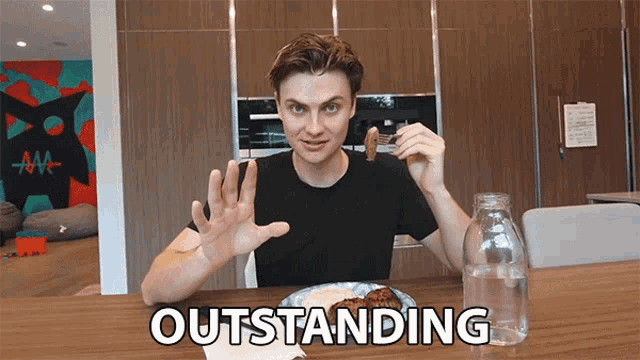 a man sitting at a table with a plate of food and a bottle of water with the word outstanding written on the table