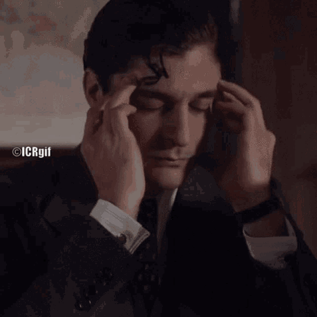 a man in a suit and tie is touching his forehead with his hands