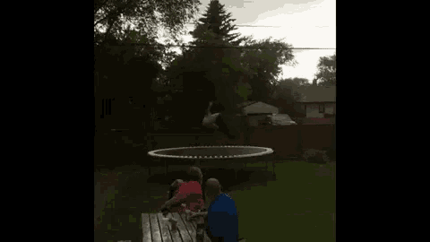 a group of people are sitting at a picnic table in front of a trampoline in a backyard .