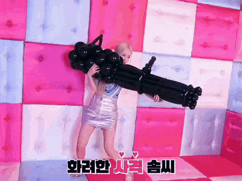 a woman is holding a gun made out of balloons in front of a pink wall