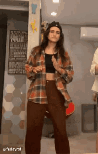 a woman in a plaid shirt and brown pants is standing in a room .