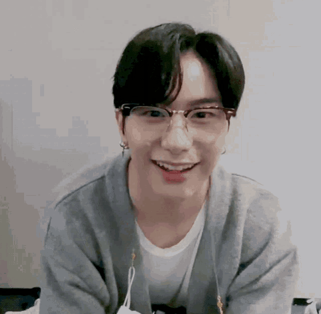 a young man wearing glasses and a gray sweater smiles