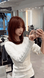 a woman in a white sweater is taking a selfie with her phone