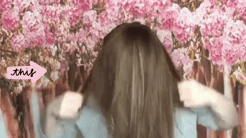 a woman is standing in front of a wall of pink flowers with an arrow pointing to the right that says this .