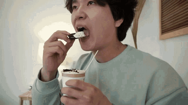a man in a blue shirt is drinking a cup of coffee and eating an oreo cookie