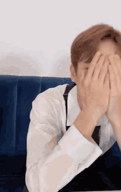 a man is covering his face with his hands while sitting on a blue couch .