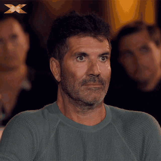 a man with a beard is sitting in front of a gold x