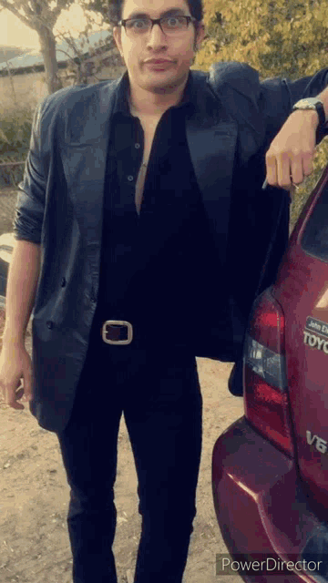 a man in a black leather jacket stands next to a red toyota