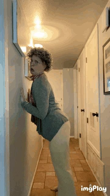 a woman is leaning against a wall in a hallway with a picture on the wall above her