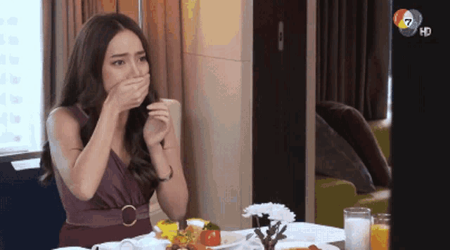 a woman covering her mouth while sitting at a table with plates of food on it