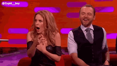 a man and a woman are sitting on a red couch laughing