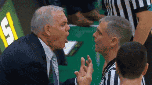 a man in a suit and tie is yelling at another man in a striped shirt