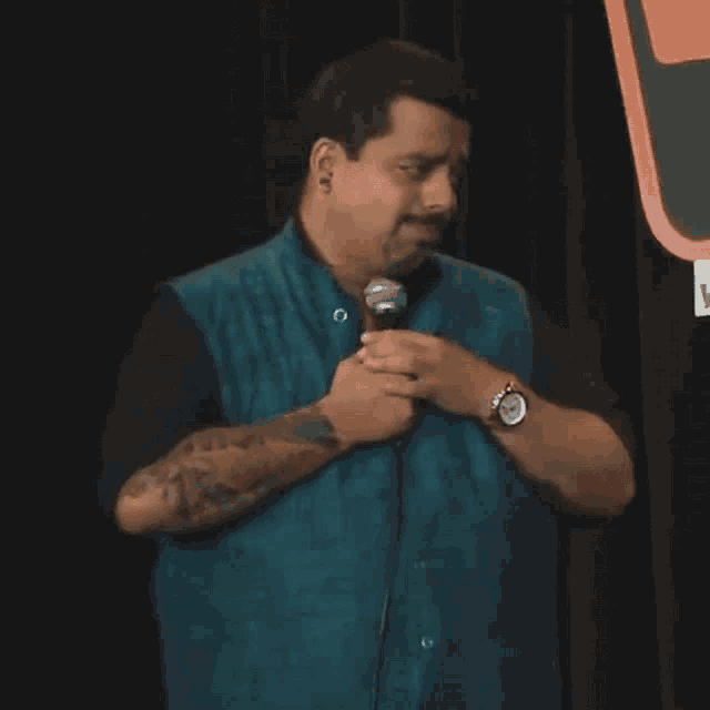 a man in a blue vest is holding a microphone and wearing a watch