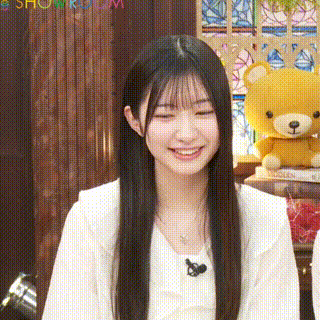 a young woman with long black hair is smiling in front of a teddy bear .
