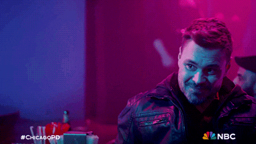 a man in a leather jacket stands in a dark room with a nbc logo on the bottom right