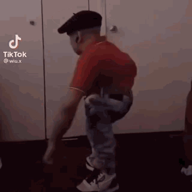 a man in a red shirt and beret is dancing in a room .