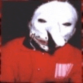 a man wearing a white mask and a red shirt is standing in front of a dark background .