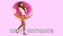 a woman is holding a large pink donut in her hands and says `` happy birthday '' .