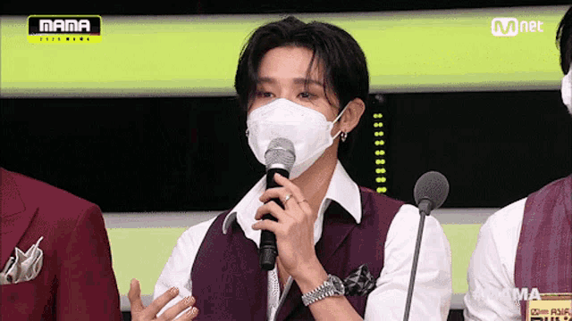 a man wearing a mask is holding a microphone in front of a mnet logo