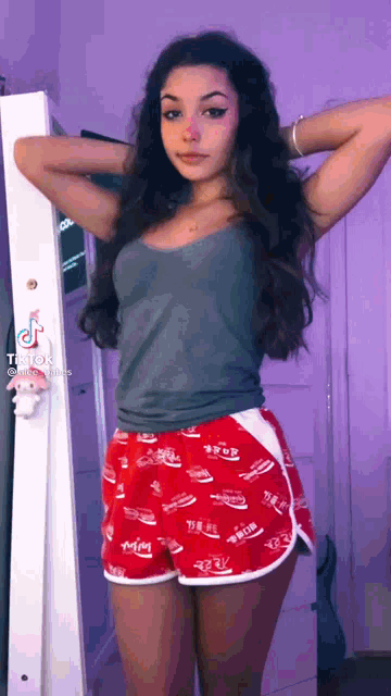 a girl in a grey tank top and red shorts is standing in front of a mirror ..