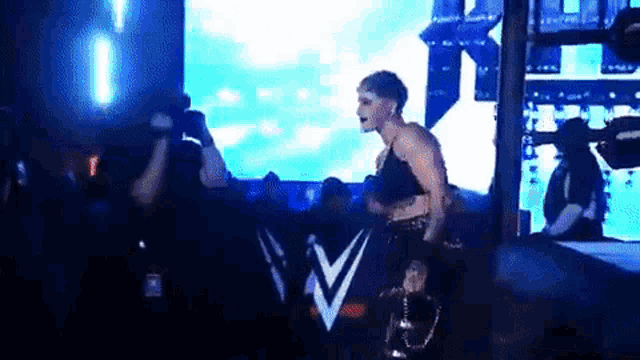 a female wrestler is walking on a stage in front of a crowd while holding a trophy .
