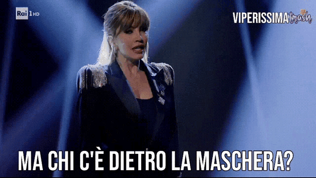 a woman in a suit stands on a stage and says " ma chi c'e dietro la maschera "