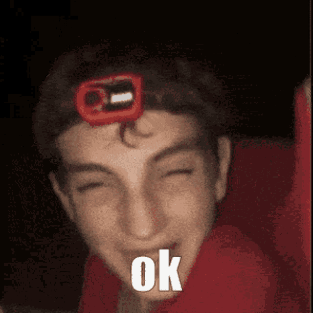 a young man wearing a red headband with a red light on it is smiling and saying ok .