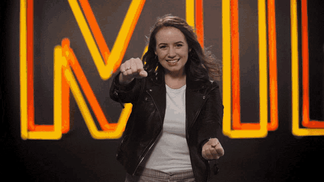 a woman in a black leather jacket points at the camera