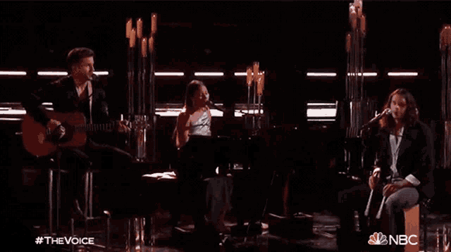 a group of people singing and playing instruments on a stage with the nbc logo in the background