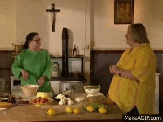 two women in a kitchen with a cross on the wall behind them