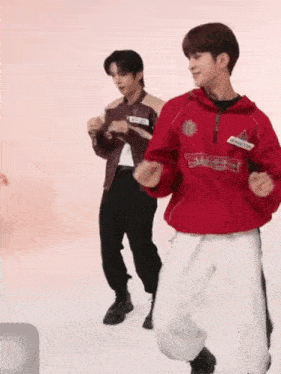 a man in a red jacket is dancing with another man in a red hoodie .
