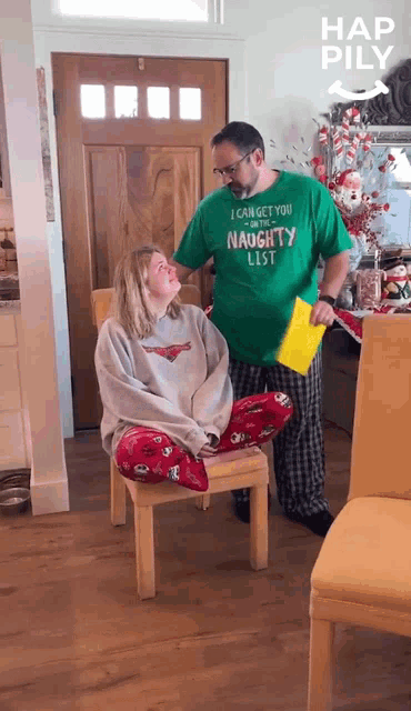 a man in a green shirt that says i can get you on the naughty list stands next to a woman in a chair