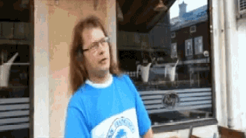 a man wearing glasses and a blue shirt stands in front of a restaurant