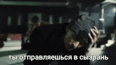 a man wearing a beanie is holding his head in his hands in a dark room .