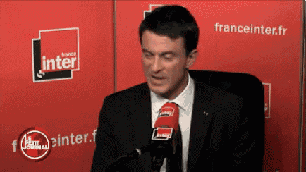 a man in a suit and tie speaks into a microphone in front of a france inter sign