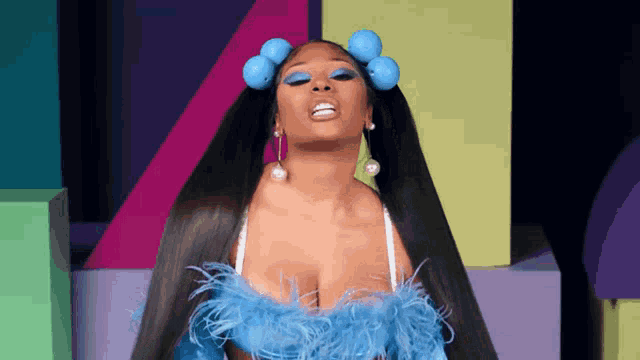 a woman with long hair and blue curlers in her hair is wearing a blue feathered top .