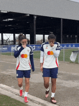 two female soccer players are walking down a sidewalk and one has the number 18 on her shirt